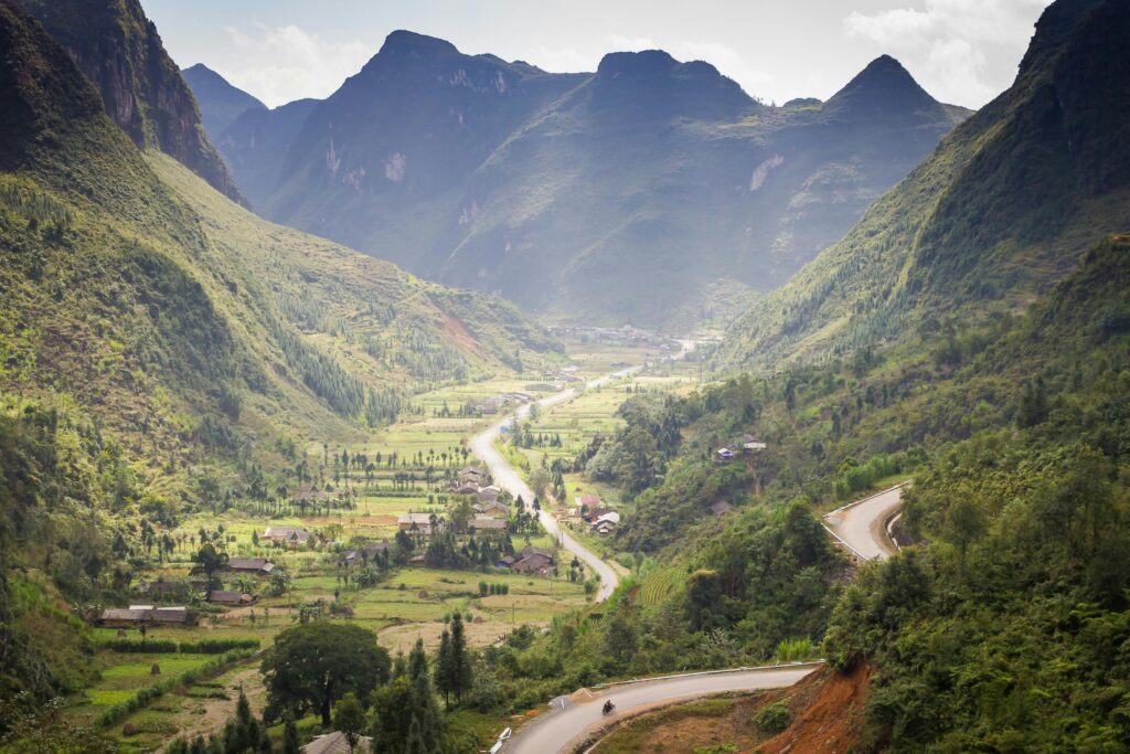 Scenic mountain valley with winding roads and lush greenery during daylight.